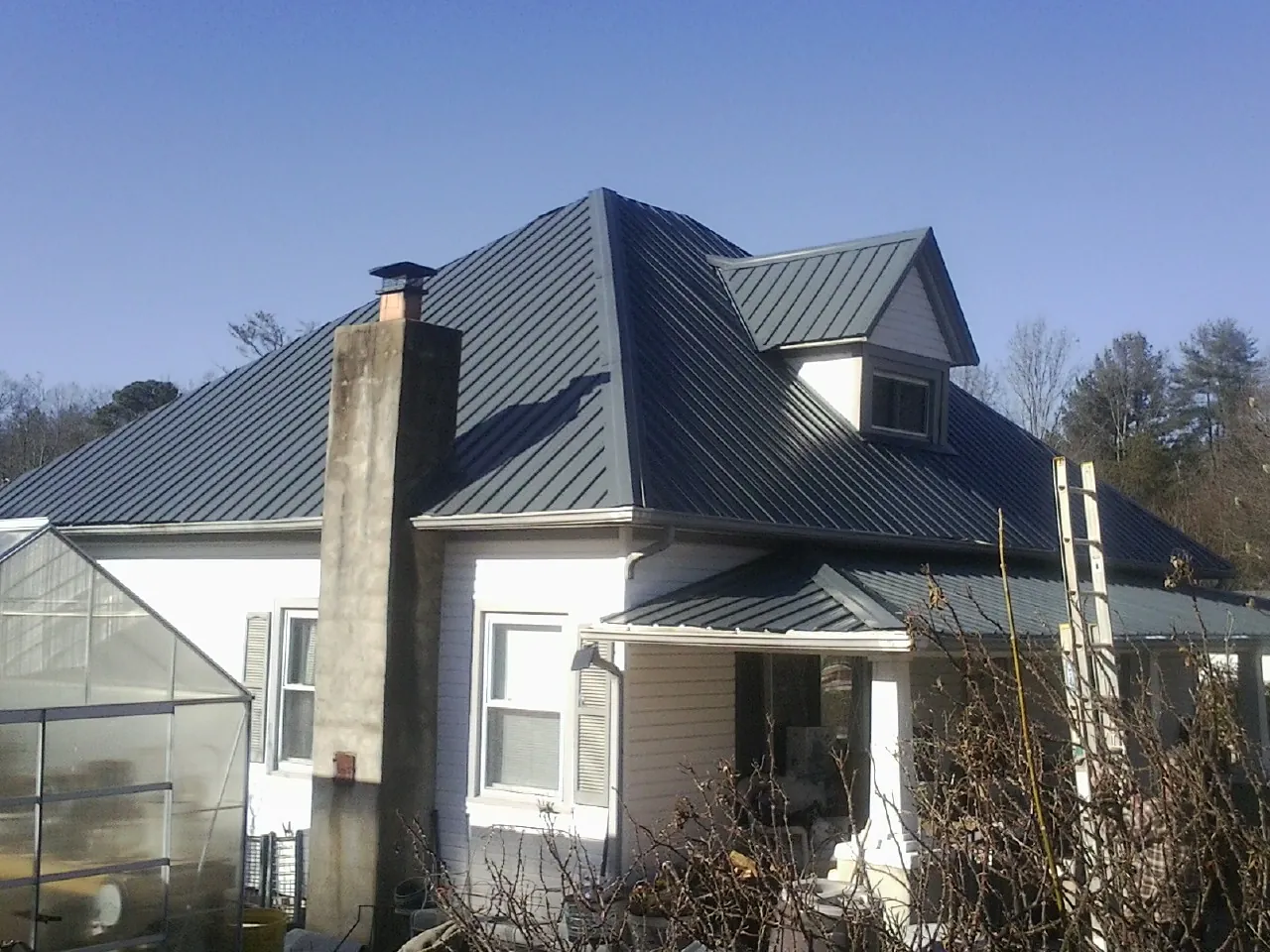 Dark blue standing seam metal roof on a white farmhouse with dormer — Slate & Tile Roof Repair by Roofing Brothers in Mays
