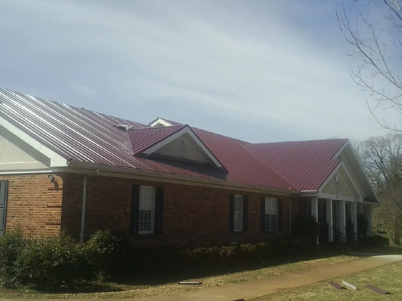 Red metal roof with gabled entries on a long brick building, from a Hail Damage Roof Repair job in Mays