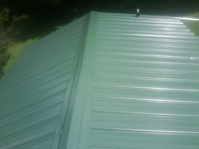 New green metal panels meeting at the ridge of a roof — Flat Roof Repair work by our crew in Mays