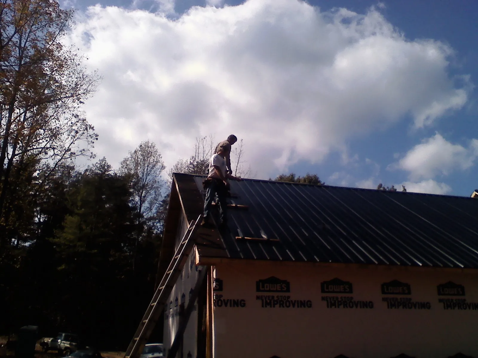 Roofer fastening dark metal panels high against a cloudy sky, from a Roof Inspection job in Mays