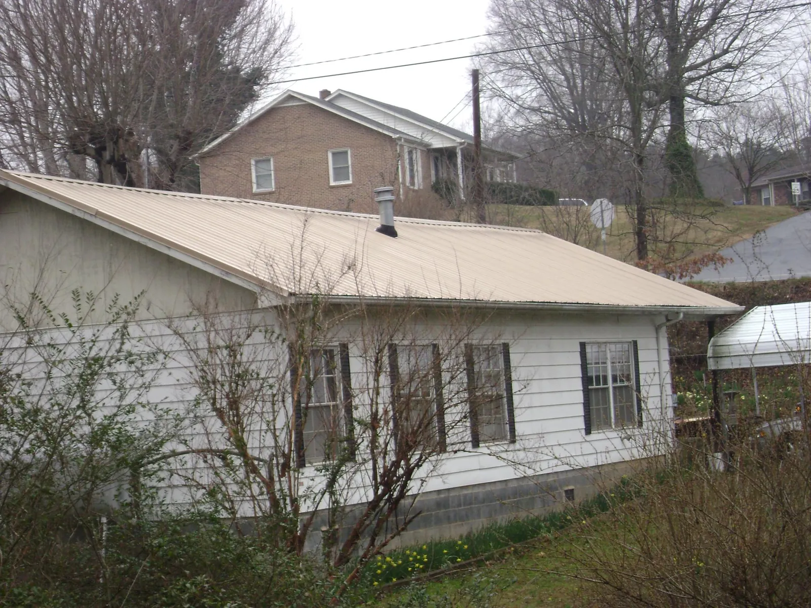 Tan metal roof on a white sided house set into a hillside — Commercial Roofing by Roofing Brothers in Mays